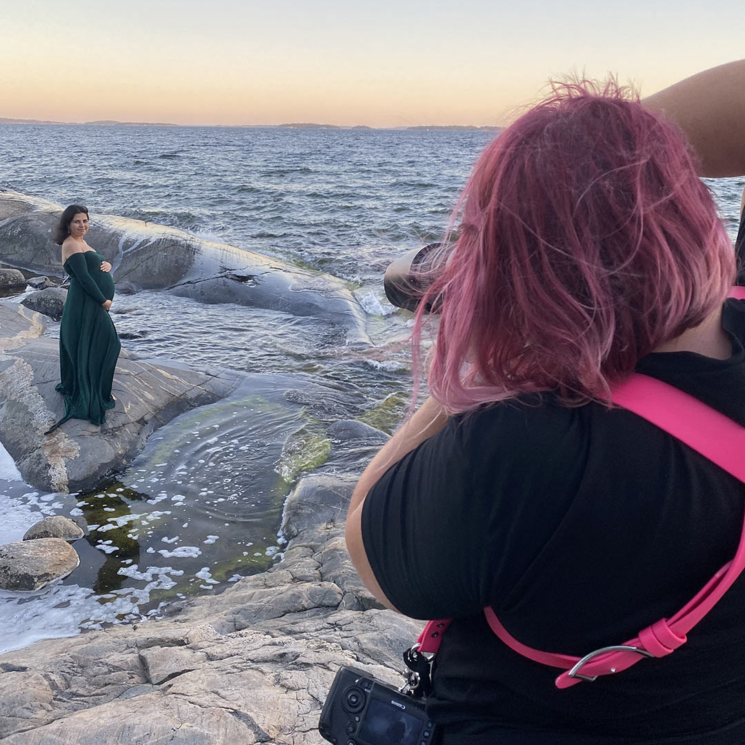 Behind the scenes-bild där gravidfotograf Linda Holmkratz syns fotografera en gravid kvinna vid havet, tagen av av den blivande fadern.