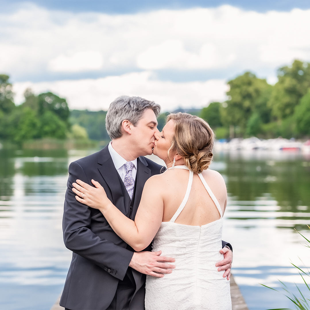 Ett bröllopspar står vid vattnet och pussas.