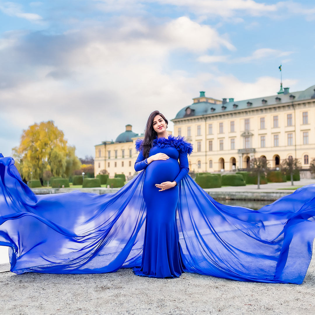 Gravidfotografering framför Drottningholms slott. Kvinnan har en blå klänning som flyger i vinden.
