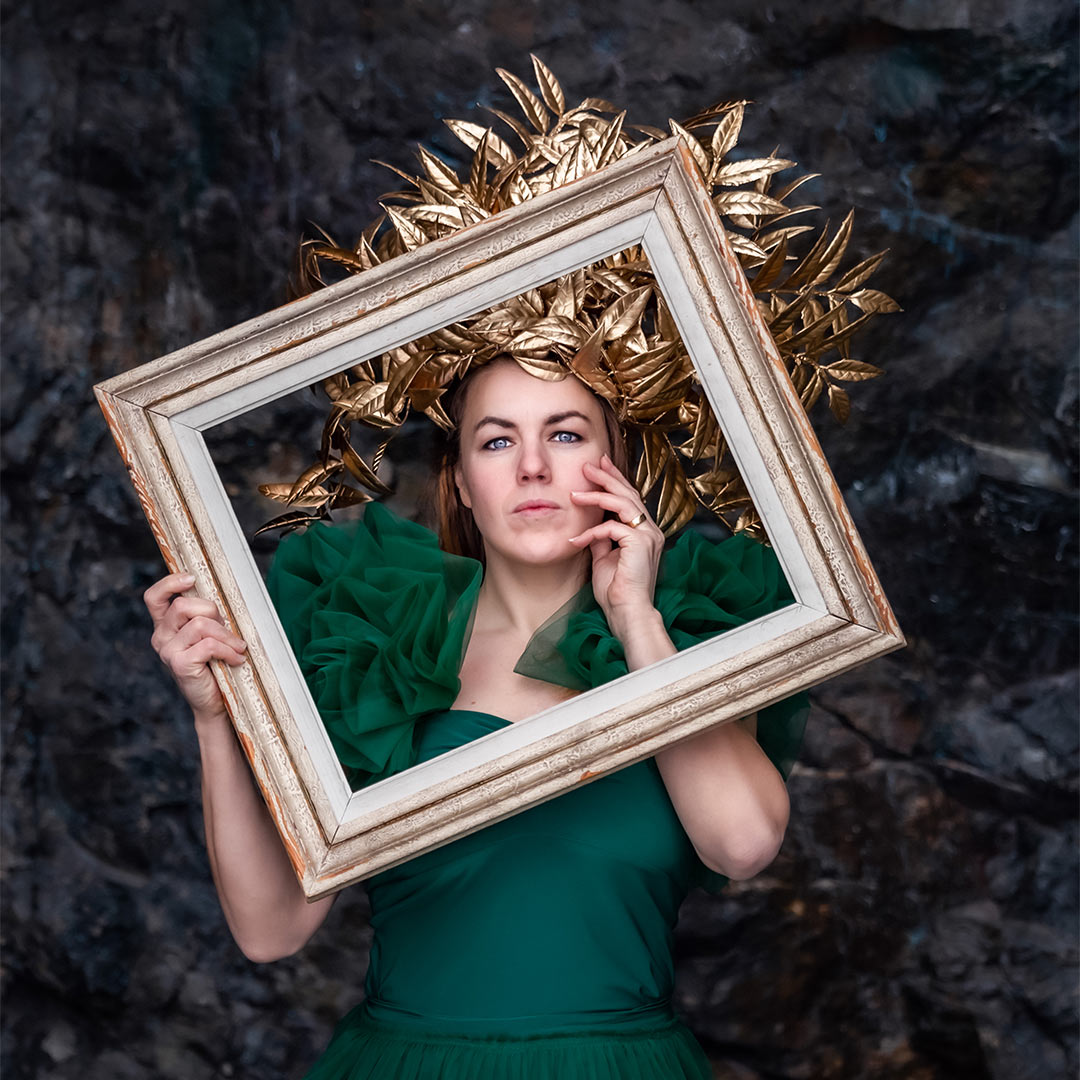 Bilden är från en kreativ porträttfotografering av en kvinna i grön klänning och med en guldkrona. Framför sig håller kvinnan en tavelram.