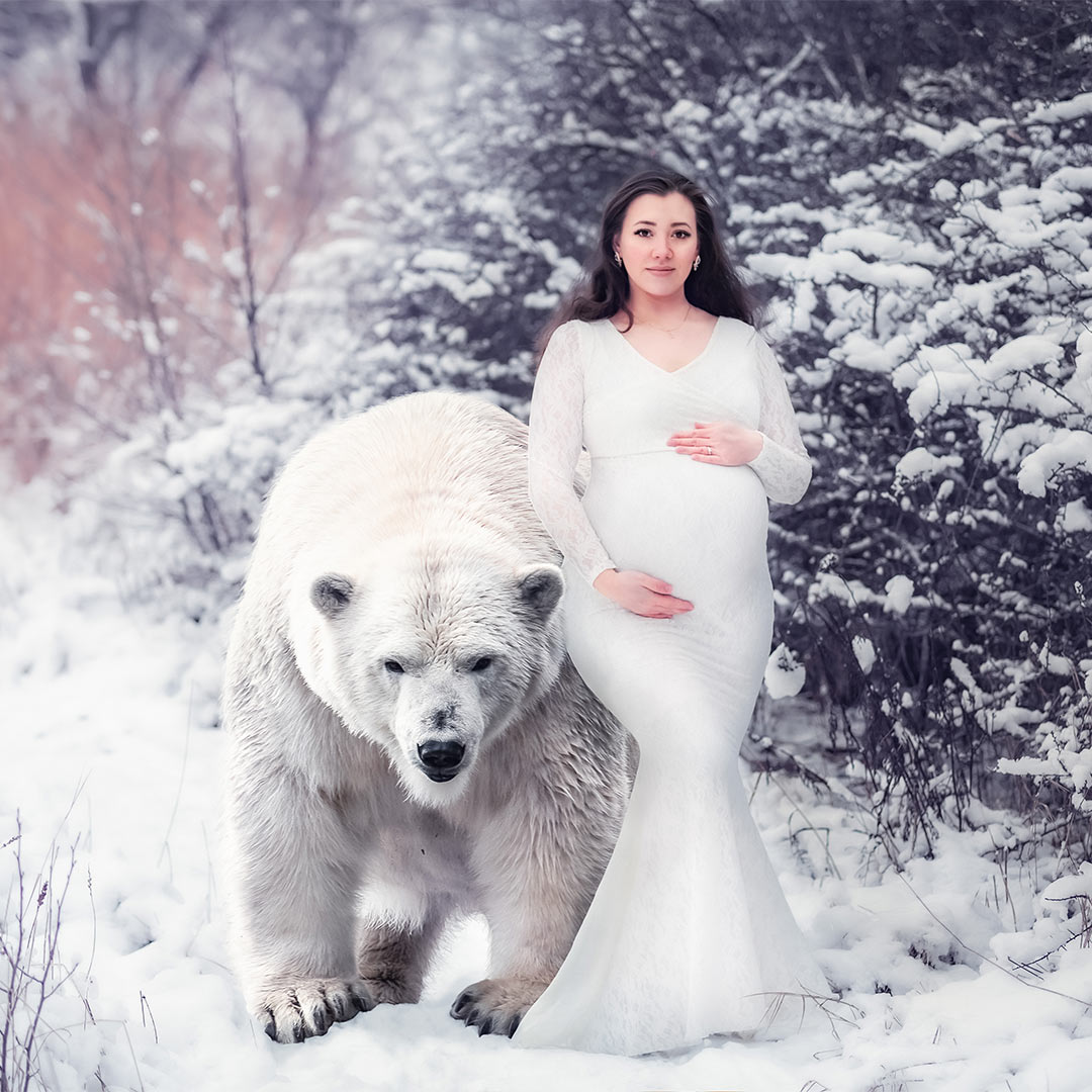 En gravid kvinna i vit spetsklänning går bredvid en isbjörn i ett snöigt vinterlandskap.