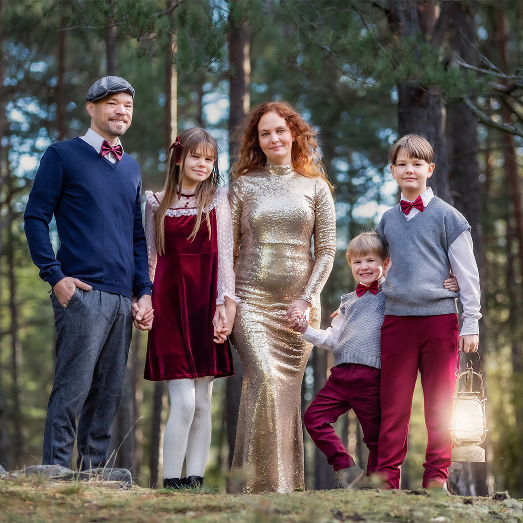 Julfotografering i barrskog med en familj i finkläder med röda detaljer.