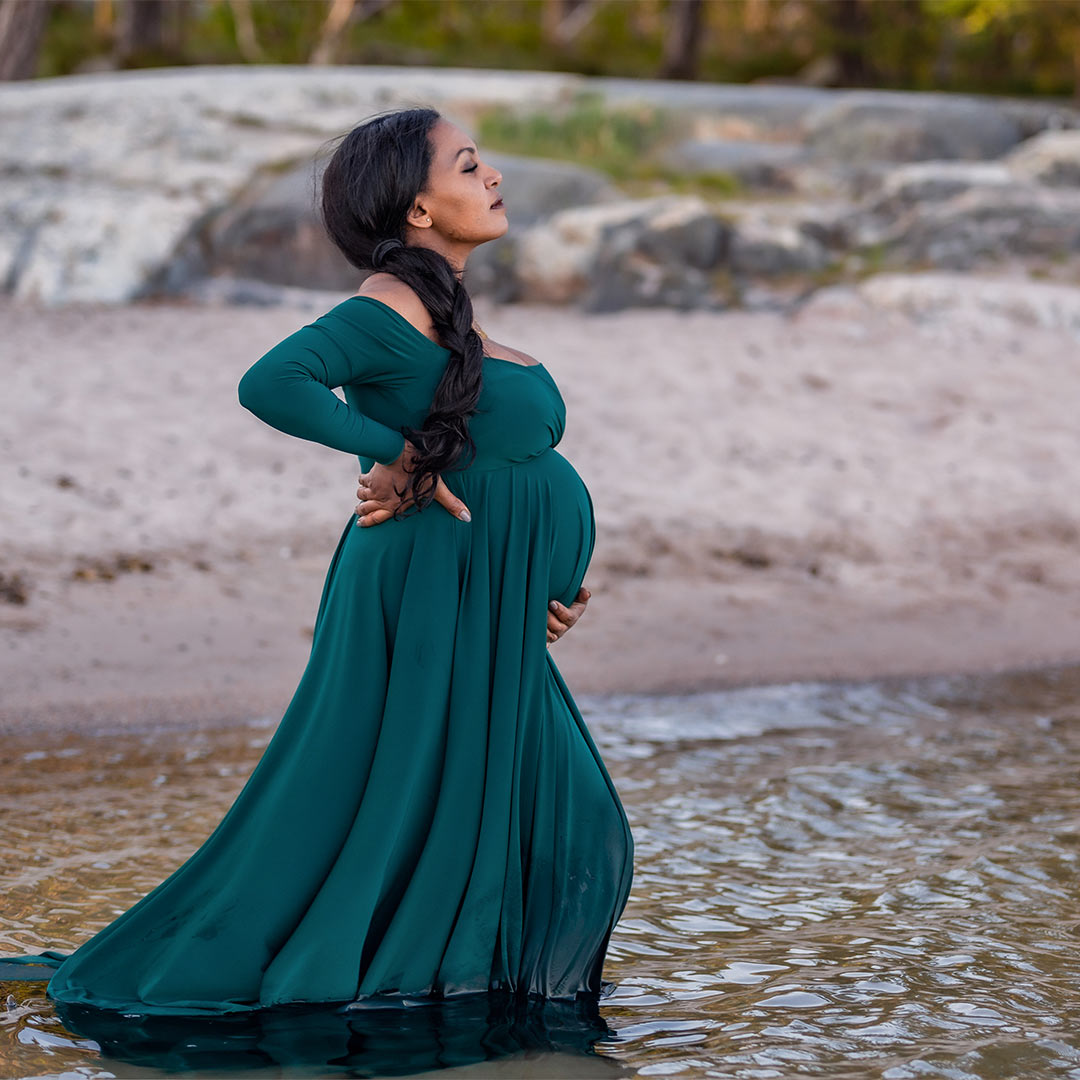 En gravid kvinna står i vattnet vid en sandstrand.