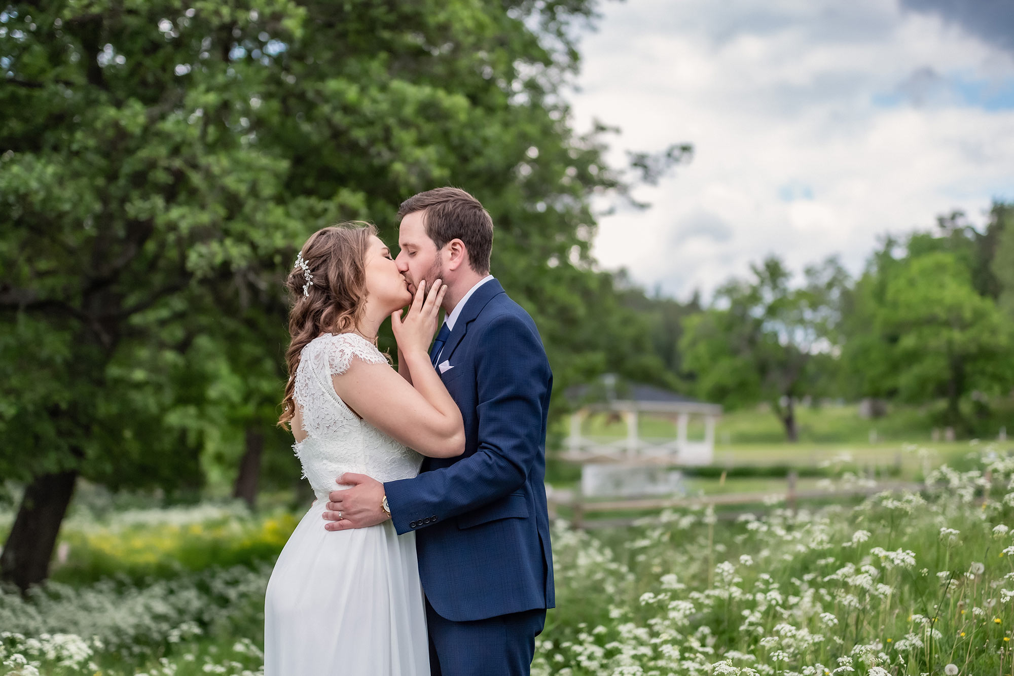 Bröllopspar pussas på en vacker sommaräng i Rönninge By i Täby. I bakgrunden syns träd och en dansbana.