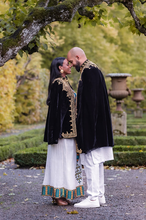 Ett förälskat par står panna mot panna under en stor gren i en slottsträdgård.